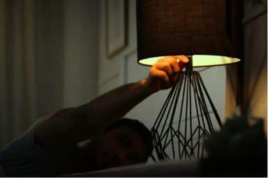 Man in bed reaching out to turn off a lamp.