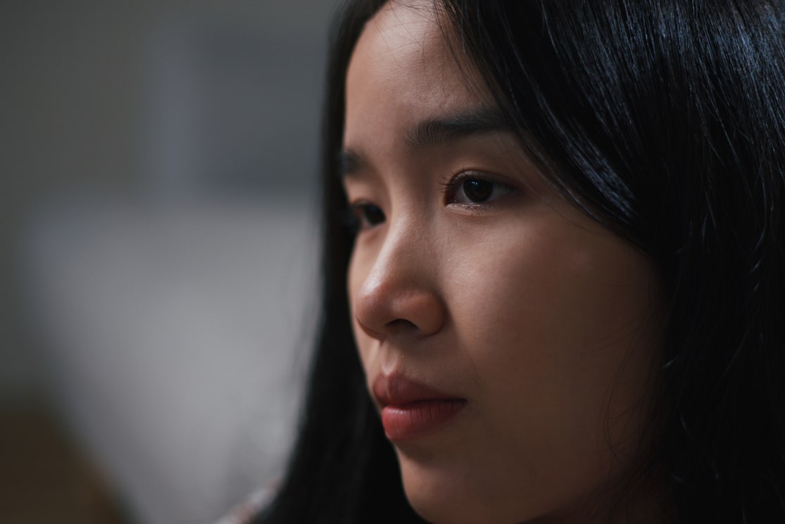 A woman with flowing black hair turns her head slightly, her expression passive aggressive as she looks away from the viewer.