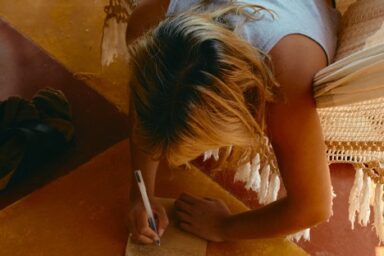 Young woman leaning over to write in journal