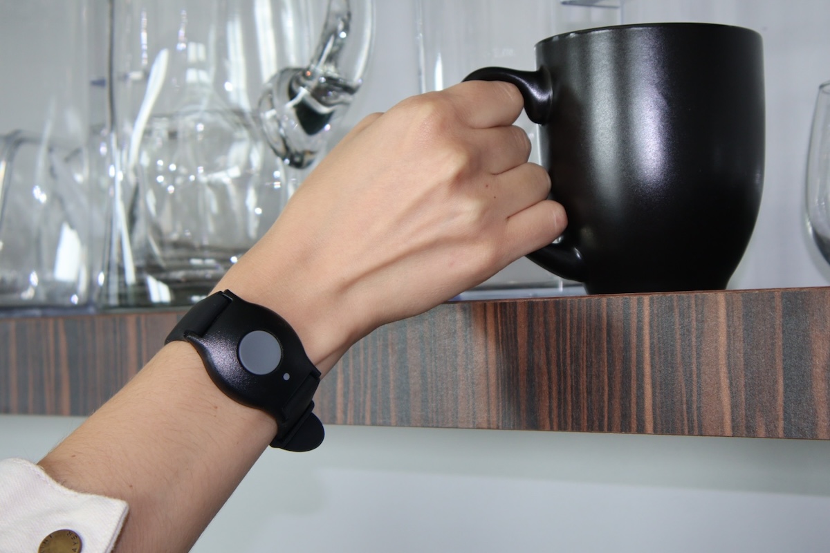 A person wearing a medical alert bracelet while reaching for a coffee cup 
