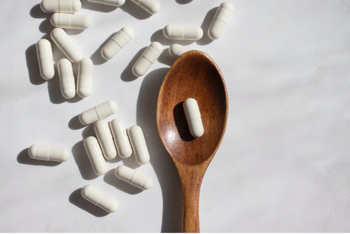 A wooden spoon sits amidst probiotic capsules