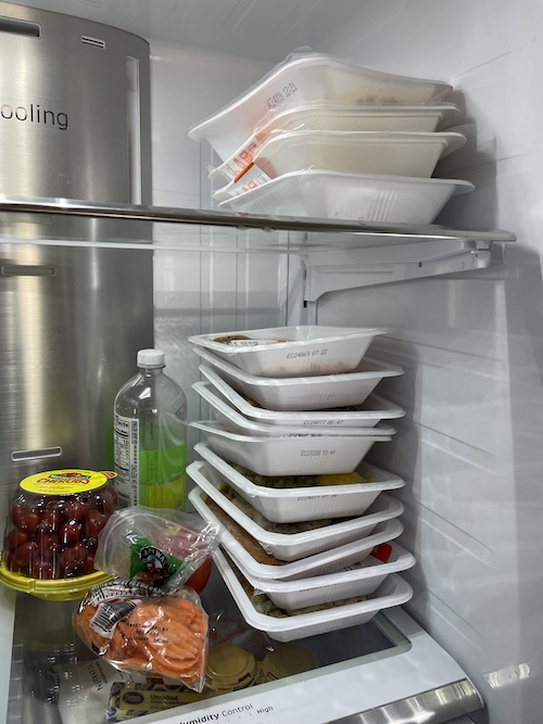  Plastic serving trays of Trifecta meals stacked in a refrigerator. 
