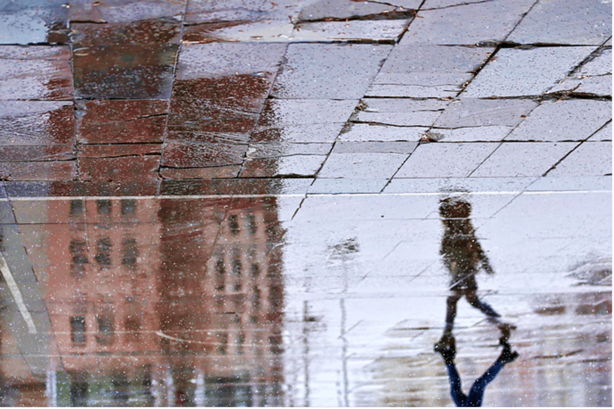 Person walking reflected in rain-soaked sidewalk